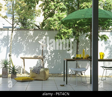 Grün Schirm über Tisch und Drahtgeflecht Stühle auf weißer Keramik gepflasterte Stadt Terrasse mit rustikalen hölzernen Pferd Stockfoto