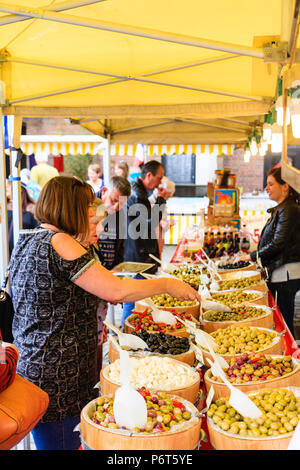 Oliven, in kleinen Fässern, verkauft auf dem Markt in der Sandwich Stadt Le Wochenende ausgeht, französische Festival. Frau, 40 Jahre, mit Schaufel einige zu kaufen. Stockfoto