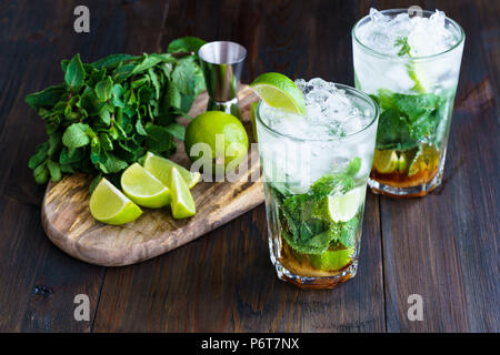 Dirty Mojito und Zutaten (frische Minze, geschnitten Kalk) auf einem dunklen Holzbrett serviert. Hohe Auflösung. Stockfoto