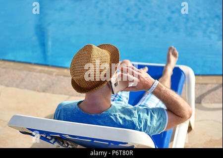 Mann mit Handy im Urlaub am Pool im Hotel, Konzept der Freiberufler arbeiten für sich selbst im Urlaub und Reisen Stockfoto