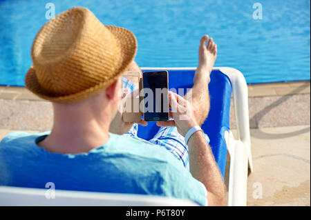 Mann mit Handy im Urlaub am Pool im Hotel, Konzept der Freiberufler arbeiten für sich selbst im Urlaub und Reisen Stockfoto