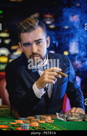 Rich handsome gut gekleideten Mann rauchen Zigarre und Roulette spielen im Casino. Konzepte von Luxus leben, Reichtum und spielende Industrie Stockfoto