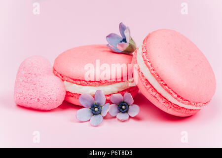 Zwei rosa Macarons mit kleinen blauen Blüten und Herzförmigen Zucker Stockfoto