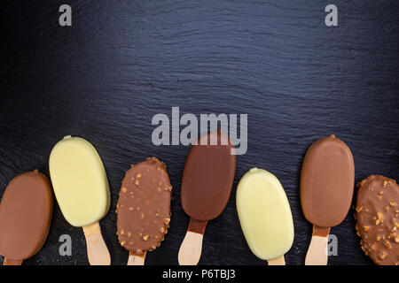 Eis auf Stick mit Schokolade auf schwarzen Stein Schiefer board abgedeckt. Stockfoto