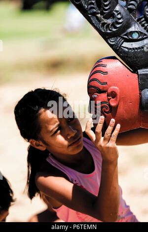 Das Mädchen schaut auf dem Gelände des Waitangi-Vertrags in Waitangi, Neuseeland, auf dem zeremoniellen Waka Taua (Kriegskanu) zu schnitzen Stockfoto