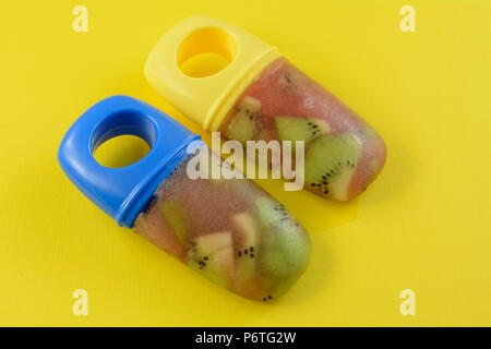 Zwei gesunde hausgemachtes Eis am Stiel von gehackte Kiwi und Cranberry Saft auf gelbem Hintergrund Stockfoto