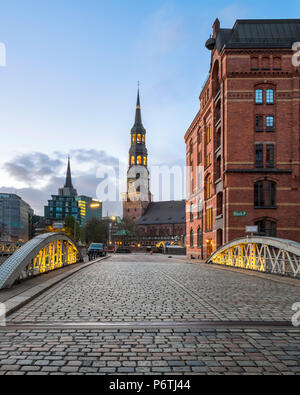 Deutschland, Hamburg, HafenCity. Historischen Lagerhäusern in der Speicherstadt Viertel und Turm der Hauptkirche Sankt Katharinen (St. Catherine's Church) in der Abenddämmerung. Stockfoto