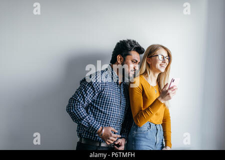 Romantische multiethnischen Paar Auswahl Badeort für ihre Flitterwochen mit Smartphone. Studio isolierte Schuß über grauer Hintergrund mit Copyspace. Stockfoto