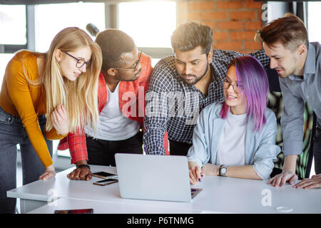 Multi-Ethnic Gruppe von Menschen, die in der Nähe von Frau mit violettem Haar, gemeinsam mit ihrem Laptop, lesen alle zusammen erstaunliche Nachrichten. Stockfoto