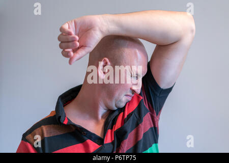 Glatzköpfige Mann, riechen Schnüffeln der Achsel, etwas stinkt schlecht. auf grauem Hintergrund. Stockfoto