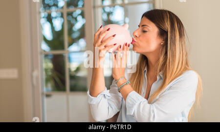 Schöne junge Frau küssen piggy Bank zu Hause, sehr glücklich mit einem Lächeln, weil der Gewinn. Geschäftskonzept. Stockfoto