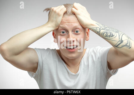 Expressive überglücklich überrascht Albino männliches Modell holding Kopf mit tätowierten Armen schockiert und Kamera mit genervt die Augen und offenen Mund. Menschliche Stockfoto
