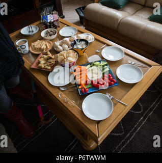 Verschiedene süße und herzhafte Fingerfood-Gerichte oder Snacks auf einem Couchtisch in der Lounge zu Hause, die für einen informellen Nachmittagstee zubereitet werden Stockfoto