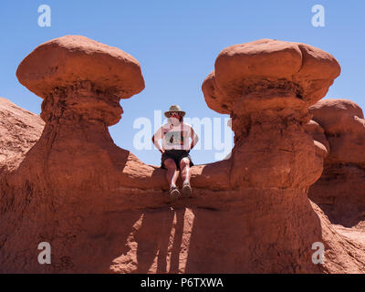 Frau sitzt zwischen zwei Goblins, Goblin Valley State Park, Hanksville, Utah. Stockfoto