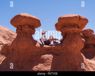 Frau sitzt zwischen zwei Goblins, Goblin Valley State Park, Hanksville, Utah. Stockfoto