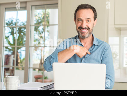 Mittleres alter Mann mit Laptop zu Hause mit Überraschung Gesicht zeigenden Finger zu sich selbst Stockfoto