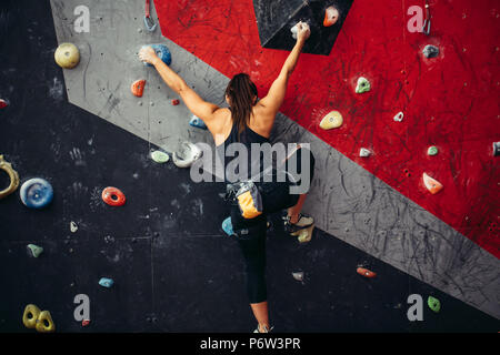 Attraktive sportliche Frau, die Bemühungen für einen großen Schritt auf eine künstliche bunte Wand mit Griffe und Haken. Stockfoto