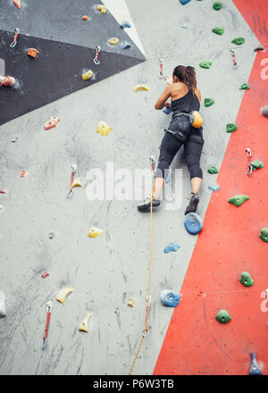 Attraktive sportliche Frau, die Bemühungen für einen großen Schritt auf eine künstliche bunte Wand mit Griffe und Haken. Stockfoto