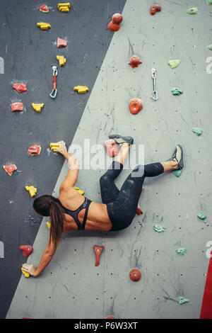 Attraktive sportliche Frau, die Bemühungen für einen großen Schritt auf eine künstliche bunte Wand mit Griffe und Haken. Stockfoto