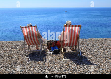 Leute sitzen auf den Liegestühlen auf einem Kieselstrand in der Nähe von Dorf Bier in Devon, an der Jurassic Coast Stockfoto
