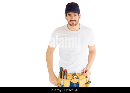 Portrait von hübscher junger Handwerker tragen Baseball Cap und Werkzeug Gürtel beim Stehen an vereinzelten weißen Hintergrund mit kopieren. Stockfoto