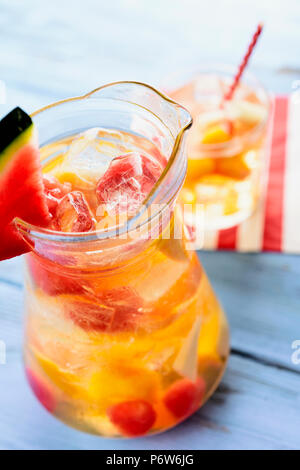 Nahaufnahme von einem Glas Krug mit erfrischenden spanische Sangria Blanca, weiße Sangria, mit frischem Obst, eine blaue, rustikalen Holztisch Stockfoto