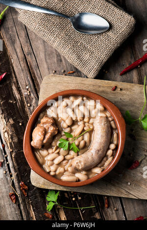 High-Angle Shot eines Steingut Schale mit einem Cassoulet de Castelnaudary, eine typische Bohneneintopf von Occitanie, in Frankreich, auf einem rustikalen Holztisch Stockfoto