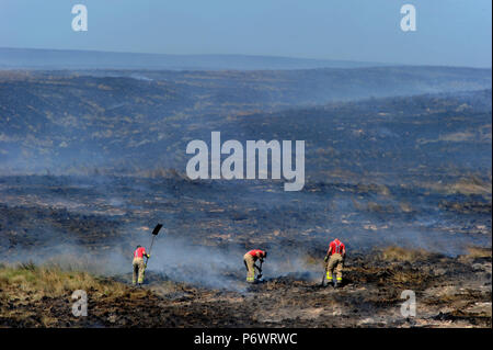 Bolton, Lancashire, UK. 2. Juli 2018. Feuerwehrmänner von Lancashire und andere Kräfte weiterhin eine riesige Moorlandschaft Feuer auf Winter Hill in der Nähe von Bolton, Lancashire in Angriff zu nehmen. Die Flamme wurde bewusst gestartet und wütet seit sechs Tagen auf einer Fläche von sieben Quadratkilometern. Feuerwehrleute in den verkohlten Landschaft schlagen die schwelenden Boden zu helfen, die Ausbreitung des Feuers. Stockfoto