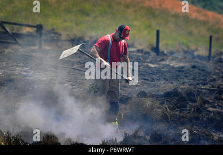 Bolton, Lancashire, UK. 2. Juli 2018. Feuerwehrmänner von Lancashire und andere Kräfte weiterhin eine riesige Moorlandschaft Feuer auf Winter Hill in der Nähe von Bolton, Lancashire in Angriff zu nehmen. Die Flamme wurde bewusst gestartet und wütet seit sechs Tagen auf einer Fläche von sieben Quadratkilometern. Feuerwehrleute in den verkohlten Landschaft schlagen die schwelenden Boden zu helfen, die Ausbreitung des Feuers. Stockfoto