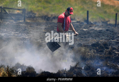 Bolton, Lancashire, UK. 2. Juli 2018. Feuerwehrmänner von Lancashire und andere Kräfte weiterhin eine riesige Moorlandschaft Feuer auf Winter Hill in der Nähe von Bolton, Lancashire in Angriff zu nehmen. Die Flamme wurde bewusst gestartet und wütet seit sechs Tagen auf einer Fläche von sieben Quadratkilometern. Feuerwehrleute in den verkohlten Landschaft schlagen die schwelenden Boden zu helfen, die Ausbreitung des Feuers. Stockfoto