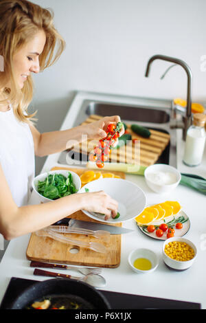 Porträt der glückliche junge hausfrau hinzufügen Cherry Tomaten in die Schüssel mit Salat. Stockfoto