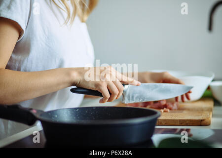 7/8-Ansicht von Frau Hände schneiden Rindfleisch auf Holzbrett. Bratpfanne Anti-haft-Pan im Vordergrund Stockfoto