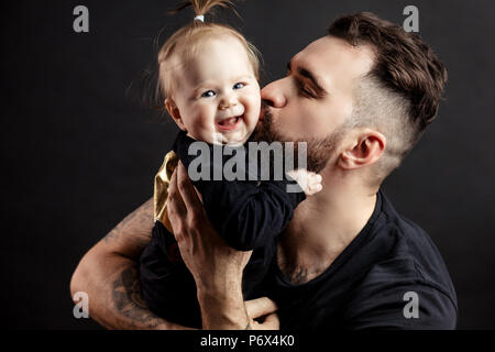 Liebevoller Vater küsste seine kleine Tochter ihre Hände bei Studio schwarzer Hintergrund mit Copyspace. Stärke, Kraft, Liebe, Zärtlichkeit Conce Stockfoto