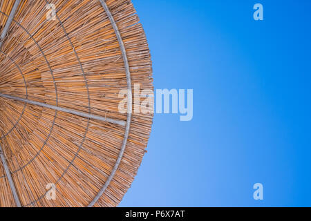 Stroh Dach der Sonnenschirm gegen den blauen Himmel. Ferienhäuser Thema. Sommer Strand, Hintergrund für eine Inschrift. Textur der schönen natürlichen Sonnenschirme aus Stroh Heu in einem tropischen Desert Resort, Stockfoto