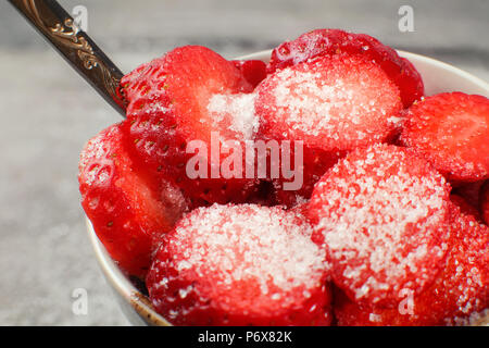 Nahaufnahme der Erdbeeren in die Kreise ausschneiden, bestreut mit Kristallzucker, in kleinen Schüssel mit silbernen Löffel, bereit zu essen. Stockfoto