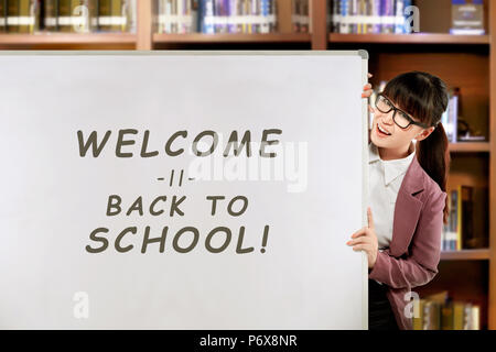 Hübsche asiatische Frau Lehrerin mit Willkommen zurück zu Schule Nachricht auf dem Whiteboard. Stockfoto