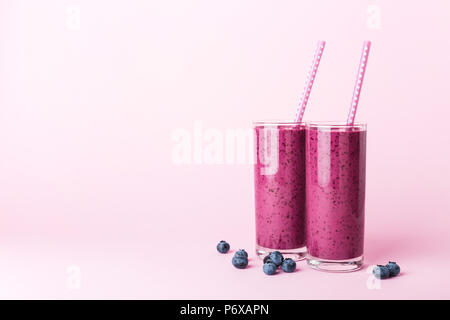 Zwei Gläser Heidelbeeren Smoothie mit Strohhalmen auf rosa Hintergrund. Gesund Sommer trinken. Stockfoto