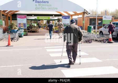 Ansicht der Rückseite des älteren Mann mit Stöcken, zu Fuß in Richtung Garten Center Stockfoto