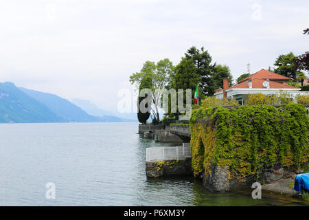 Zaun mit Efeu in der Nähe von House mit Italien Flagge, den Comer See und Alpen Berg im Hintergrund. Stockfoto