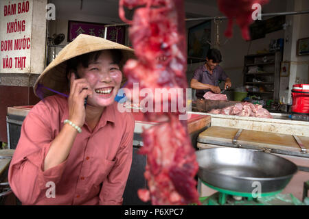 Frau Metzger Fleisch verkaufenden und am Telefon mit konischen Hut in Can Tho, Vietnam Stockfoto