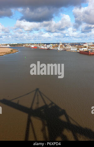 Port mit Kränen auf den Fluss Daugava in Riga, der Hauptstadt Lettlands, mit einem Schatten auf dem Wasser mit Wellen von ein Kran für die Verladung von Containern Stockfoto