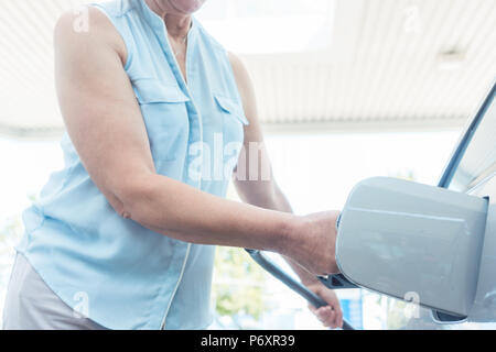 Active Senior lächelnde Frau beim Befüllen des Gastanks von ihrem Auto Stockfoto