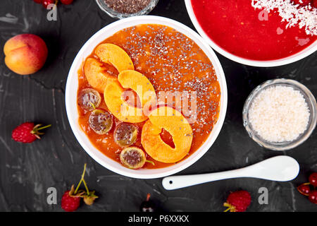 Smoothie Schalen. Gesundes Frühstück Schüssel auf schwarzen Hintergrund. Aprikose Smoothie mit Blackberry und Chia Samen. Himbeer Smoothie mit Erdbeere und Co Stockfoto