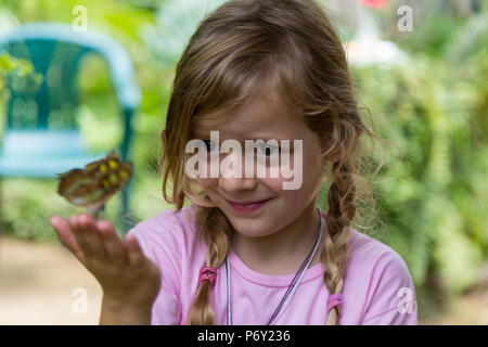 Grinsend blonde Mädchen mit einem gelben beschmutzt Schmetterling in der Hand. Selektive konzentrieren. Medium close up. Stockfoto