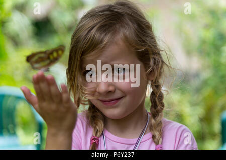 Gerne blonde Mädchen mit einem gelben beschmutzt Schmetterling in der Hand. Selektive konzentrieren. Close Up. Stockfoto