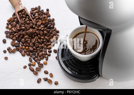 Kaffeemaschine füllt eine Tasse Kaffee auf Tisch mit Kaffeebohnen Stockfoto