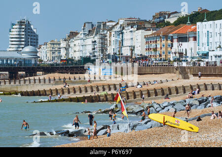 Sonnenanbeter und Schwimmer an einem heißen Tag im Juni am Strand von Hastings, East Sussex, UK, mit Gebäuden und Marine Court im Hintergrund Stockfoto