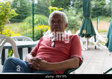 Portrait eines älteren Mannes, Sitzplätze in einem Hinterhof Terrasse. Drei viertel länge. Geringe Tiefenschärfe. Stockfoto