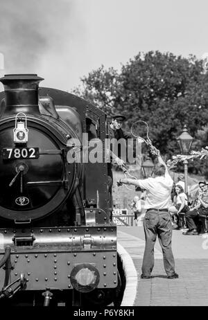 Schritt zurück zu 1940 Wochenende: vintage Lokomotive dampft in Arley Station als Einweisende auf der Plattform bereit, Token mit Feuerwehrmann Austausch wartet. Stockfoto