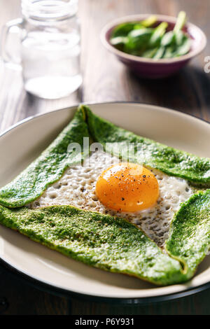 Glutenfreie Spinat Crepe mit frischem Ei auf einem hölzernen Hintergrund Stockfoto